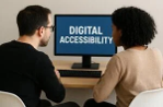 A man and a woman sitting at a desk, looking at a computer monitor displaying the text 'DIGITAL ACCESSIBILITY.'