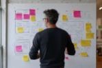 Person standing in front of a whiteboard covered with colourful sticky notes and diagrams, appearing to analyse or organise the information.