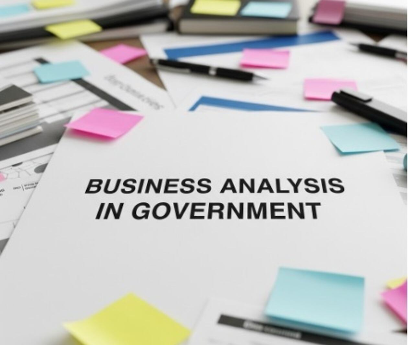Document titled ‘Business Analysis in Government’ on a desk, surrounded by papers, notebooks, pens, and colorful sticky notes.