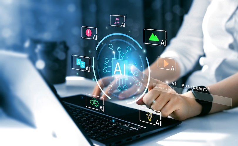 Person using a laptop with a futuristic artificial intelligence interface displayed above the keyboard. A glowing AI chip icon is surrounded by floating icons representing translation, voice, music, image generation, video, automation, and virtual assistant capabilities, illustrating AI-powered productivity and digital tools.